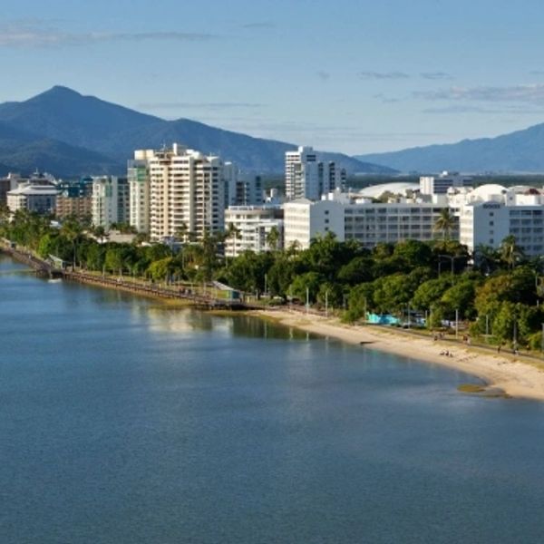 Coastal cityscape with buildings, greenery, and mountains in the background.