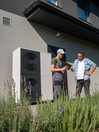 Homeowner and technician review heat pump settings outside. 