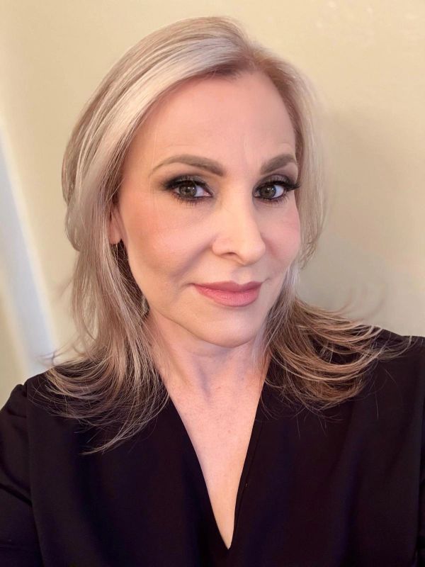 Confident woman with light blonde hair and natural makeup in black attire.