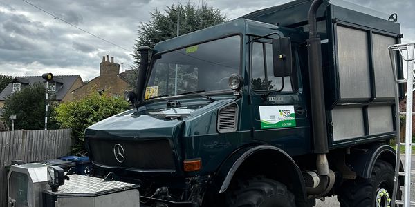 A dark green Mercedes truck parked outdoors under a cloudy sky.