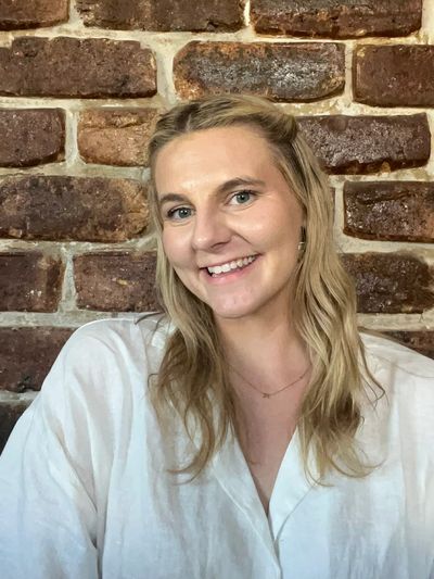 Smiling woman in a white shirt poses against a rustic brick wall.