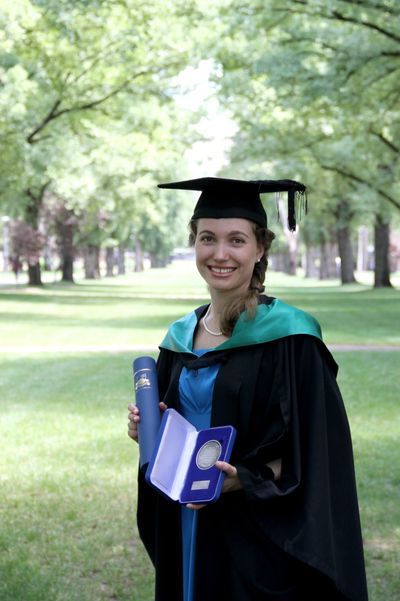 A woman wearing a graduate gown and cap is holding her degree and a medal. Credit: Robert Kirby