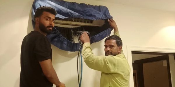 Two men working on an air conditioning unit inside a room.