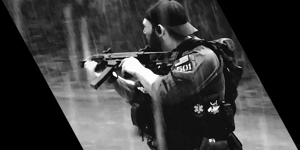 Black and white image of a soldier aiming a rifle, wearing tactical gear and a backwards cap.