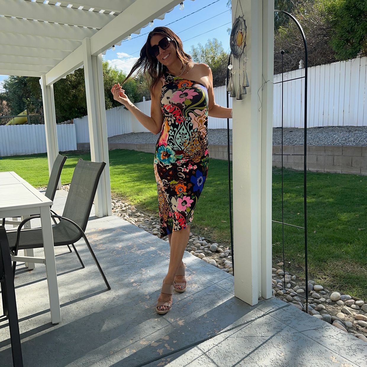 Woman in a colorful floral dress posing on a patio under a pergola.