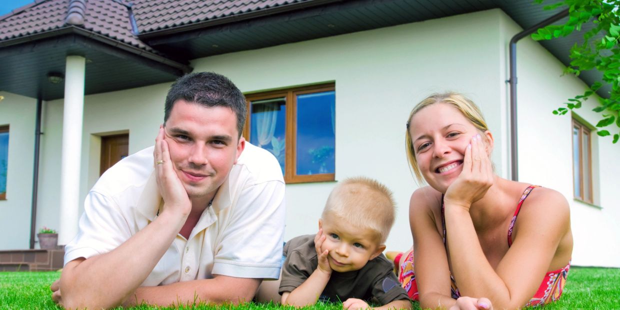 Happy family lying on green grass outside their house.