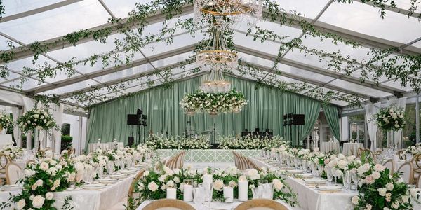 Elegant wedding reception setup with white flowers and greenery under a transparent tent.