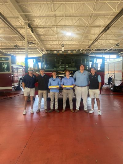 Six young men posing in front of an Oxford fire truck inside a fire station.