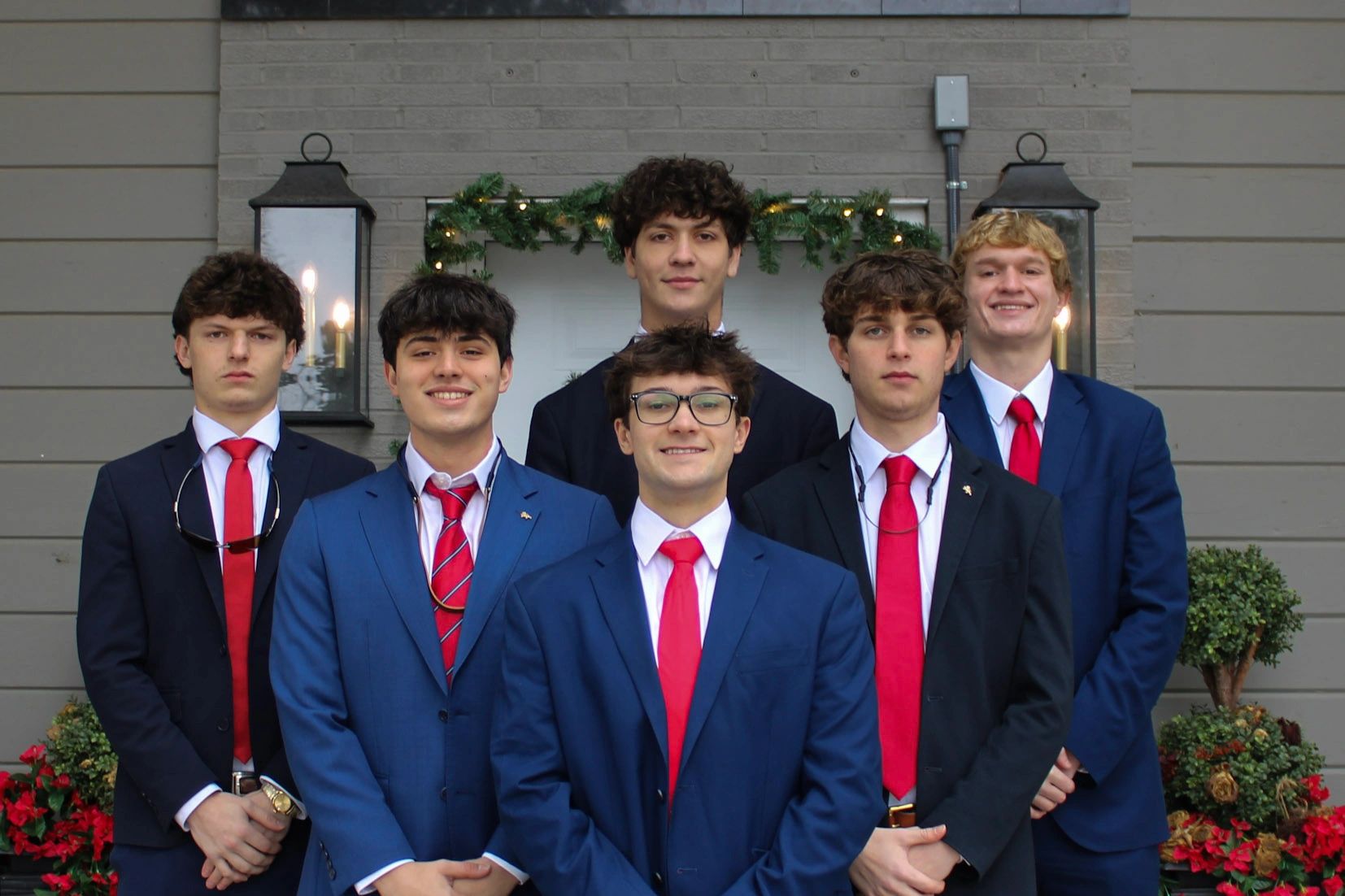 Six young men in suits with red ties standing in front of a Delta Kappa Epsilon sign.