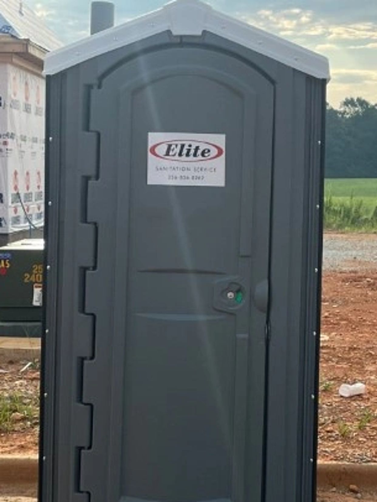 A portable toilet on a construction site with a partly built house in the background.