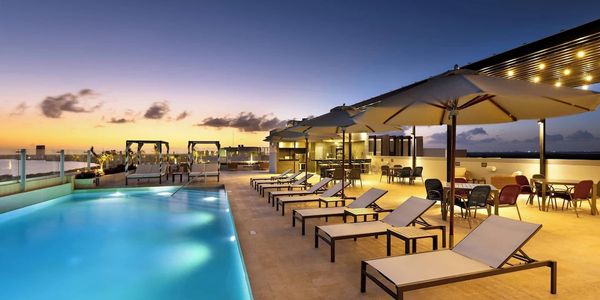 Luxurious rooftop pool area with lounge chairs and umbrellas at sunset.