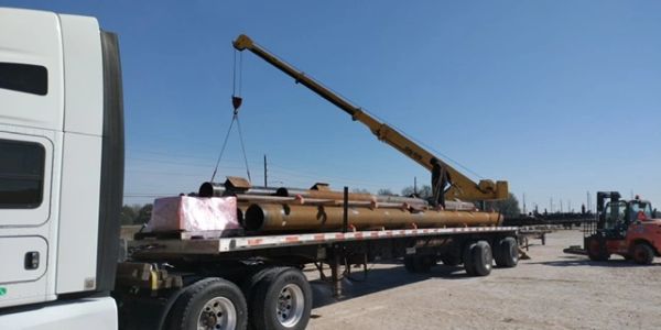 Truck trailer loaded with pipes being lifted by a crane.