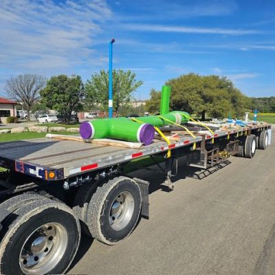 Flatbed trailer carrying large, colorful pipes.