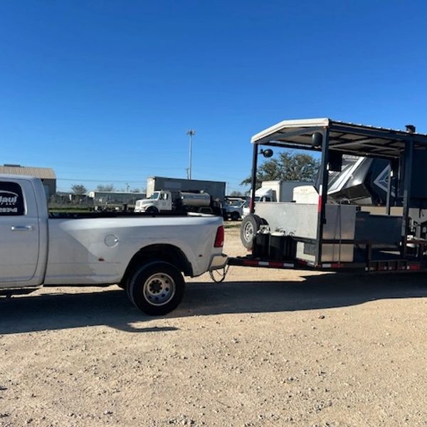 White pickup truck towing a trailer with equipment under a clear blue sky.