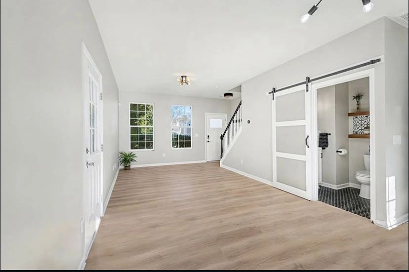 Bright empty room with wooden flooring and sliding barn door bathroom.