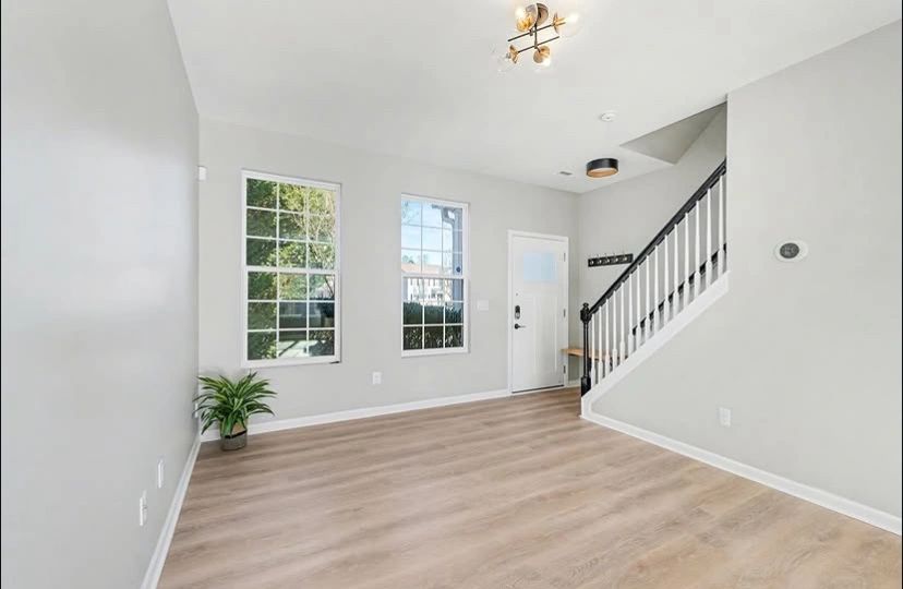 Bright, empty living room with light wood flooring and staircase.