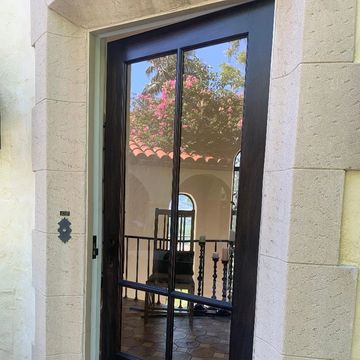 Reflected view of a chair and patio through a glass door with black frame.