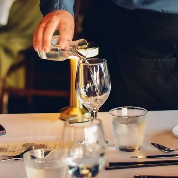 A server pouring water into a glass.