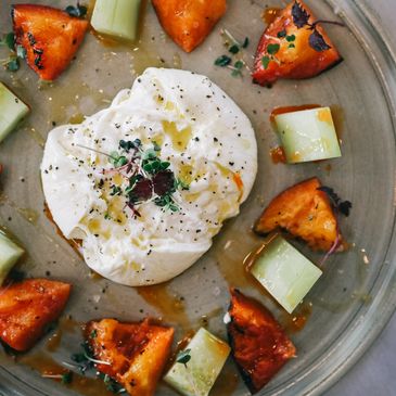 plated dish featuring creamy burrata cheese, caramelized peaches, cucumber, and microgreens.