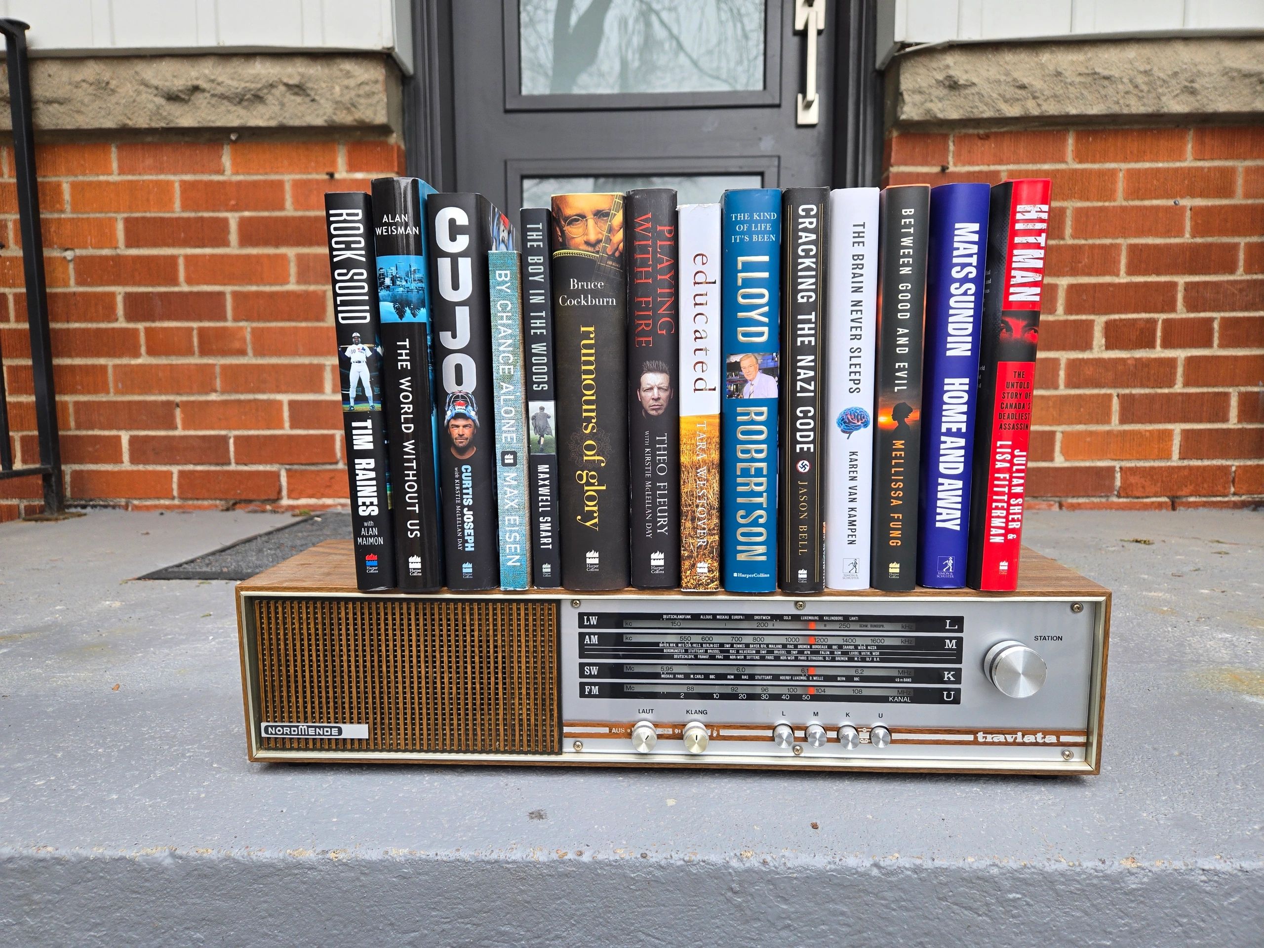 Books lined up on a vintage Nordmende Traviata radio with a brick wall background.