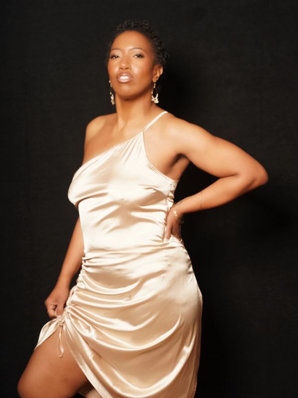 Woman in a silky beige dress posing confidently against a black background.