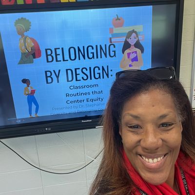 Woman smiling in front of a screen displaying a presentation on classroom routines and equity.