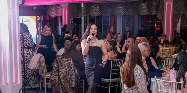 Woman in black dress singing at a formal event with seated audience.