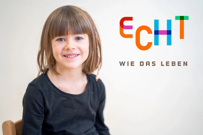 Smiling young girl with colorful hair beads, next to the German phrase "Echt wie das Leben."