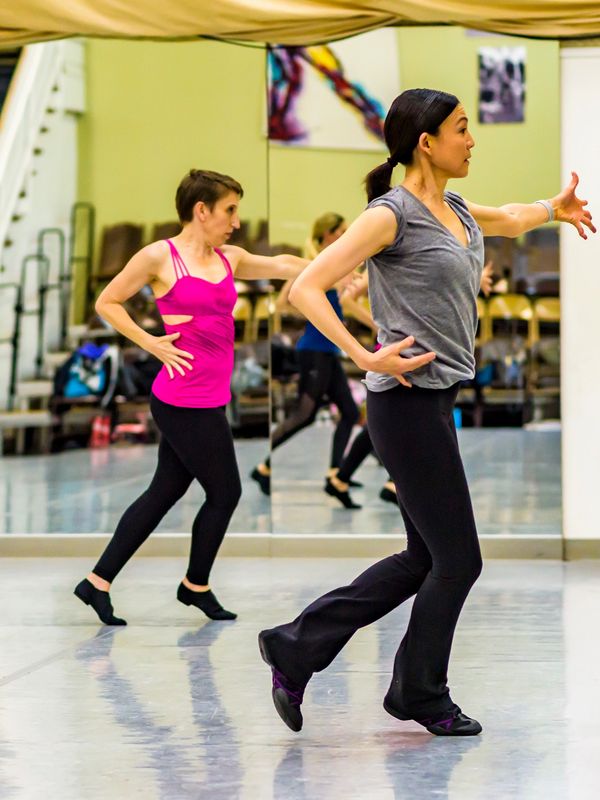 Two women practicing dance moves in a studio with mirrored walls.