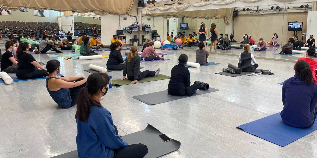 A group of people in a fitness class sitting on mats listening to an instructor.