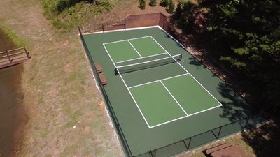 Aerial view of an outdoor pickleball court surrounded by trees and a pond.