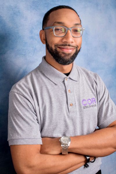 Smiling man with glasses in a gray polo shirt.