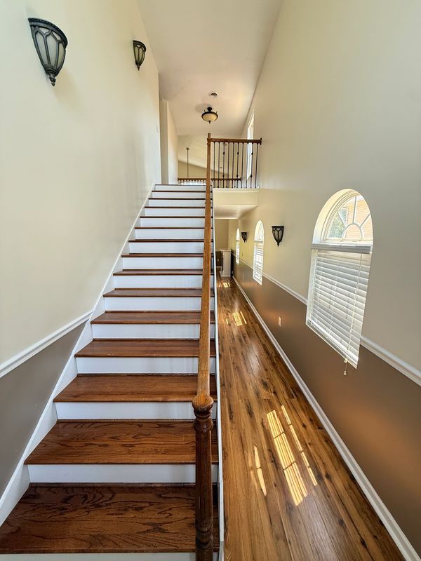 A wooden staircase and a long hardwood floor hallway with wall-mounted lights.