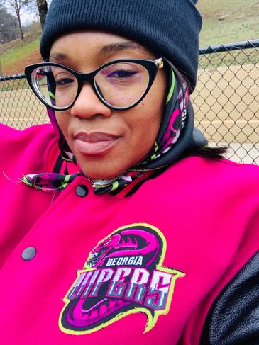 Woman in black beanie and glasses wearing a bright Georgia Vipers jacket.