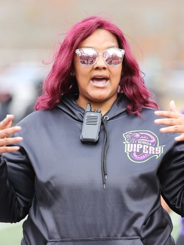 Woman with vibrant hair and reflective sunglasses speaking energetically.
