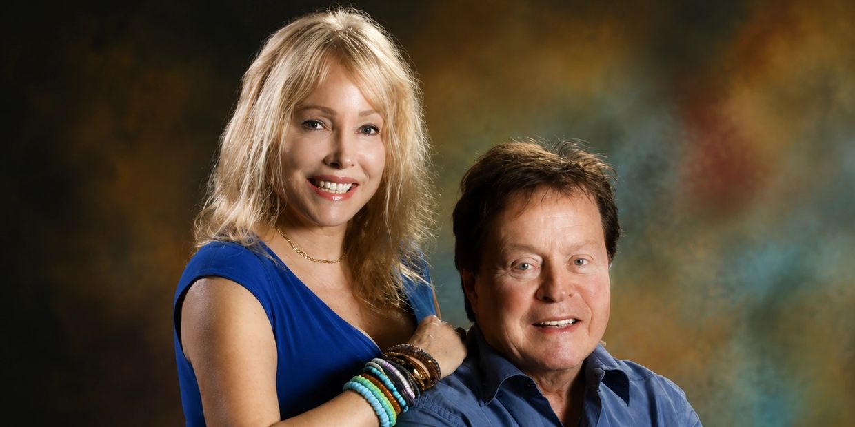 A smiling couple posing against a warm-toned backdrop.