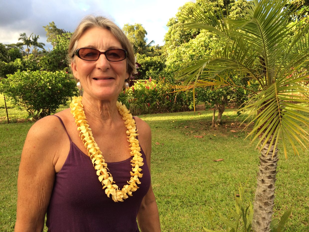 Smiling woman wearing sunglasses and a yellow lei in a lush garden.