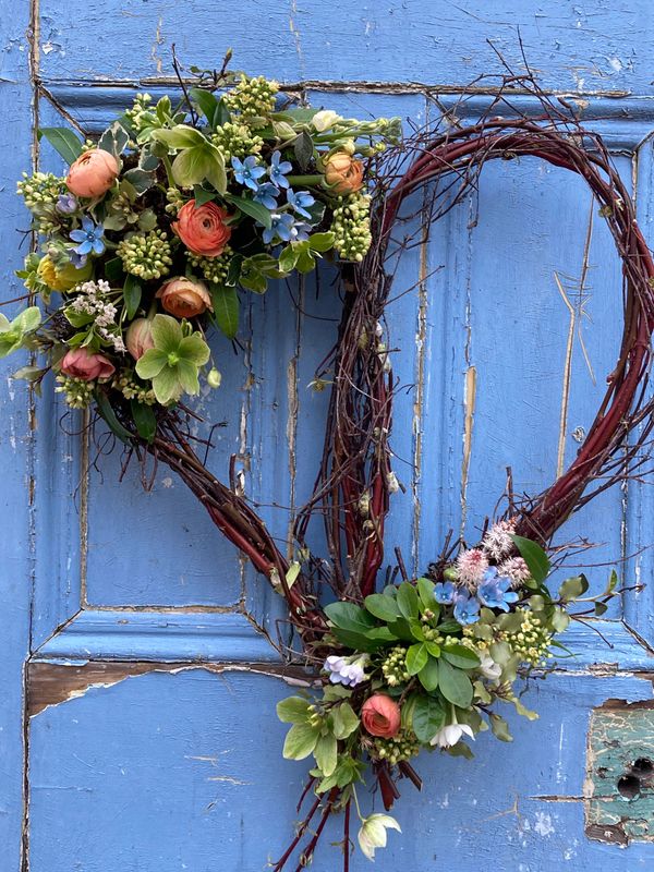 Heart-shaped twig wreath adorned with colorful flowers on a weathered blue door.