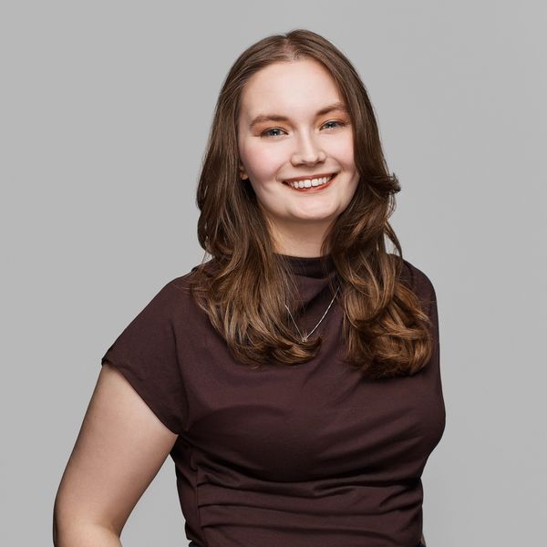 Young woman smiling confidently with brown hair and a dark top.