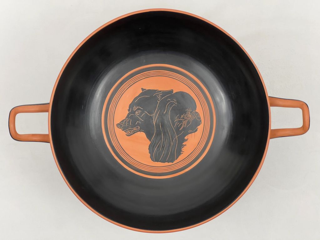 Ancient Greek-style ceramic bowl with dual animal head design in black and orange.