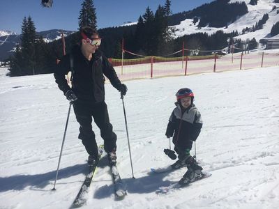 Dad and child on the ski slope in the sunshine, wearing skis and ski jackets and trousers