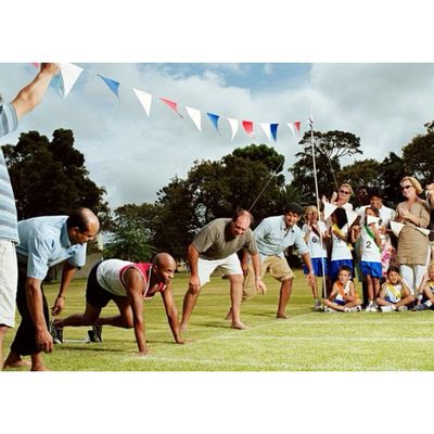 dads lining up for a race at child's school sports day, families cheering them on to win