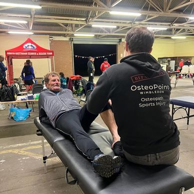 Older man in tracksuit top and trousers receiving osteopathy support during through the darkness run