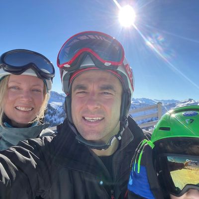 Husband, wife and son wearing ski gear and helmets, in the sun on a ski slope in Austrian Alps