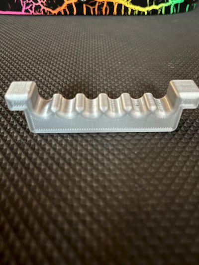 Silver plastic object with six rounded indentations on a textured black surface.