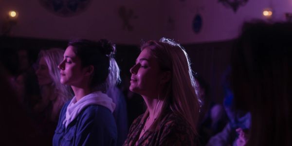 Two women with closed eyes in purple lighting.