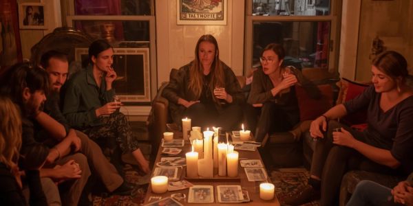 Group of people sitting in a circle with candles and tarot cards.