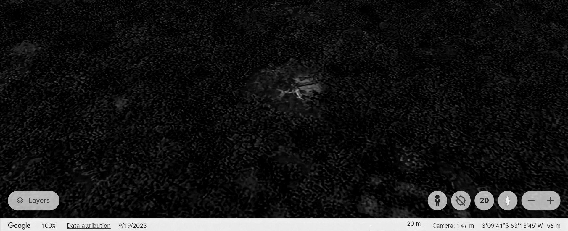 A dark, grainy aerial view of a small illuminated area in a dense forest.