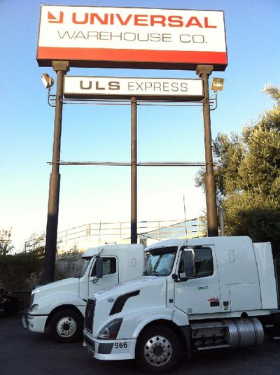 Two ULS Express Trucks parked in front of the Universal Warehouse CO. sign