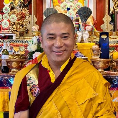 Smiling Buddhist monk in traditional robes inside a decorated temple.